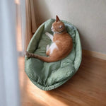A ginger cat curled up in a green oval pet bed with a padded rim.